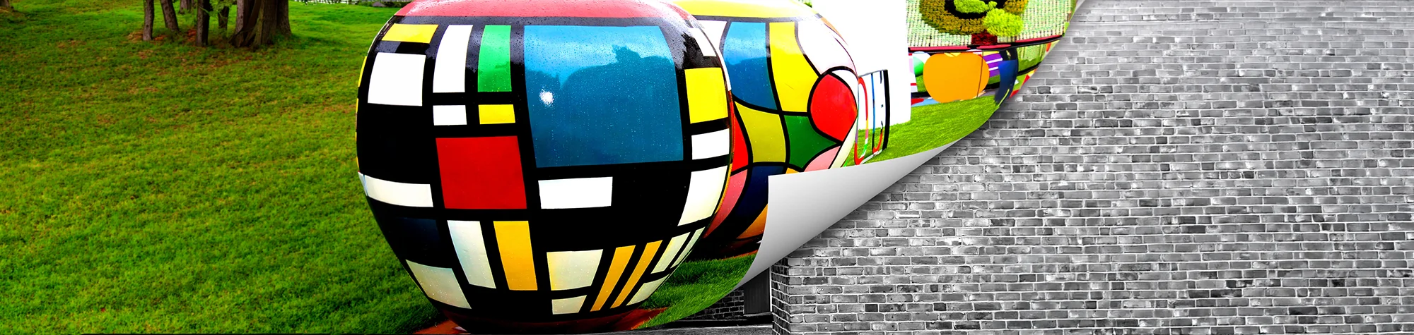 A wide panoramic image showing a Photoshop page curl effect peeling back a colorful pattern to reveal a black and white brick wall.